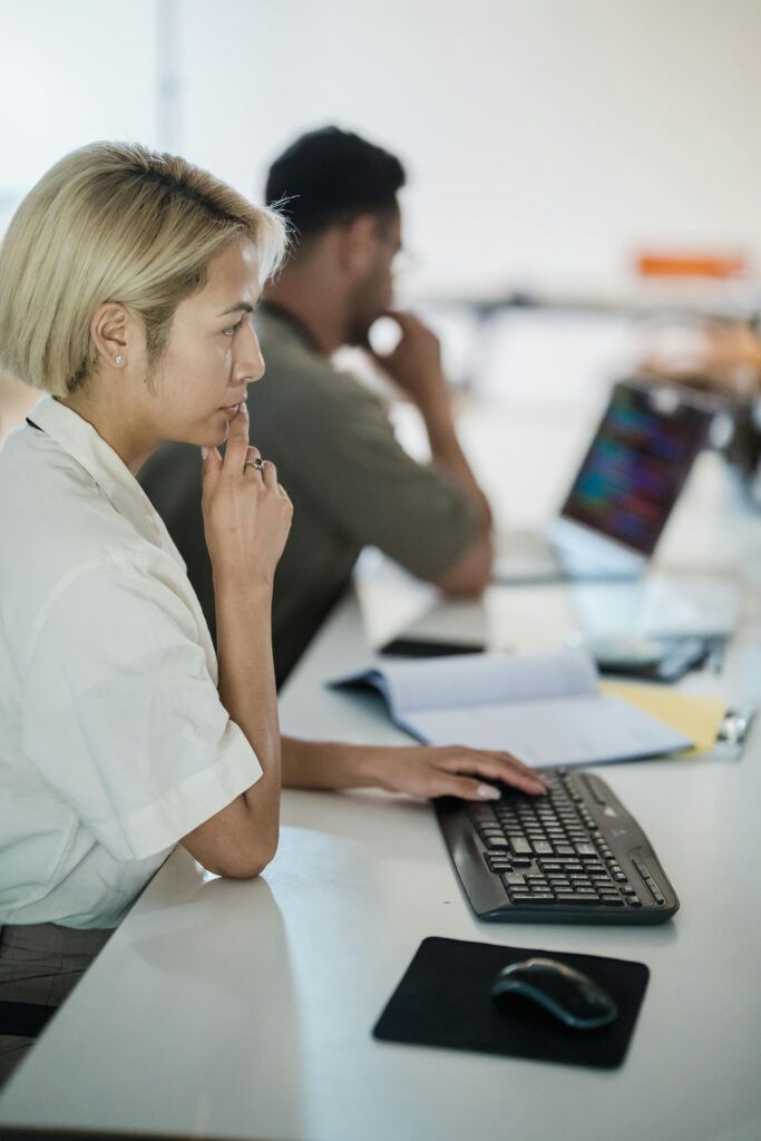 Professional office workers concentrating on tasks with computers at a shared desk setting.